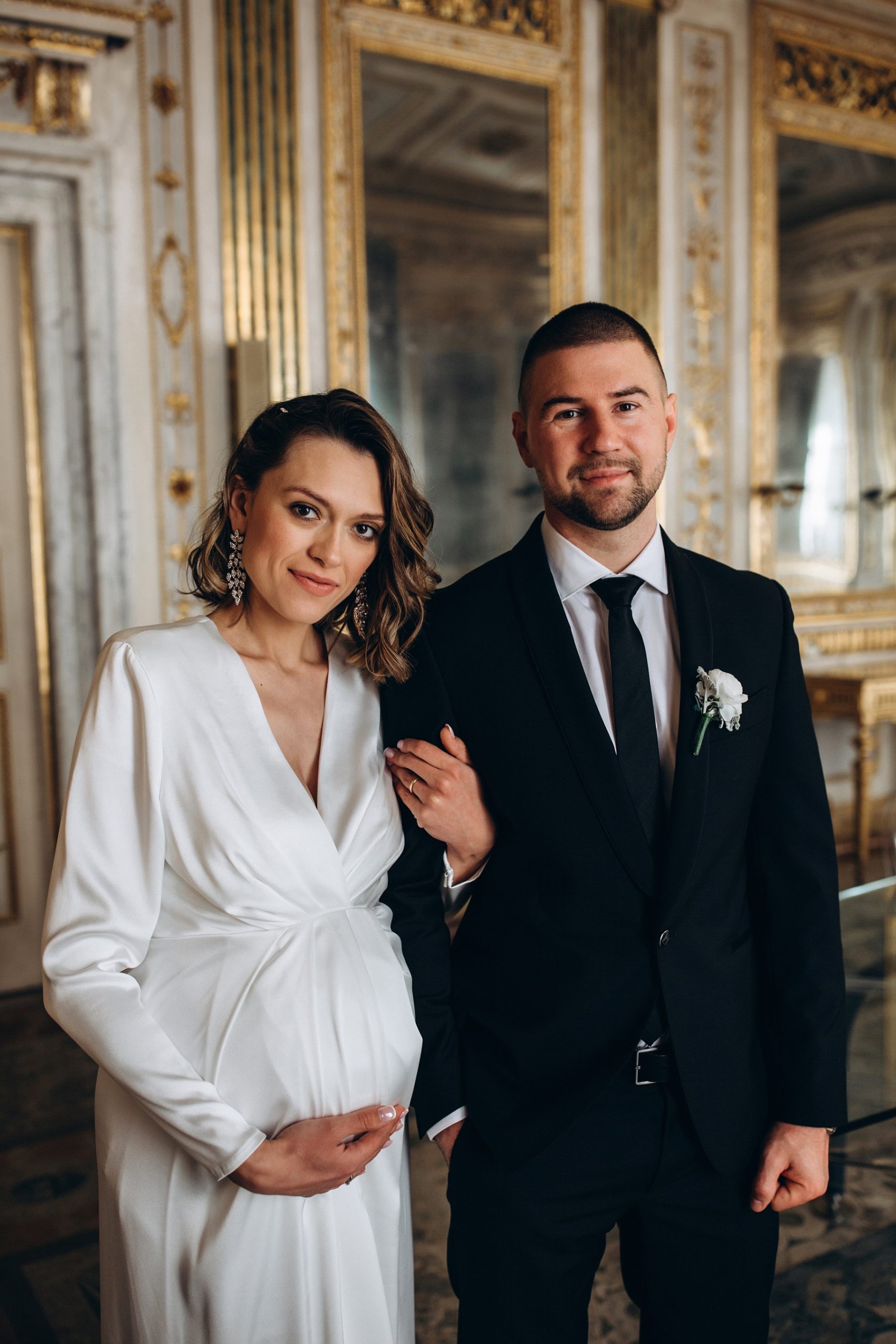 Panna Młoda pokazująca ciąży pokazująca brzuch w prostej sukni ślubnej z Panem Młodym ślub
