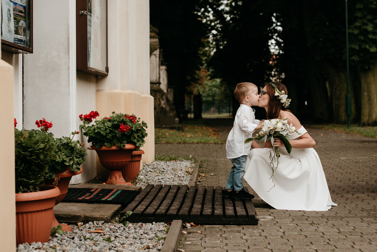 Panna Młoda z bukietem kwiatów i dzieckiem przed salą weselną