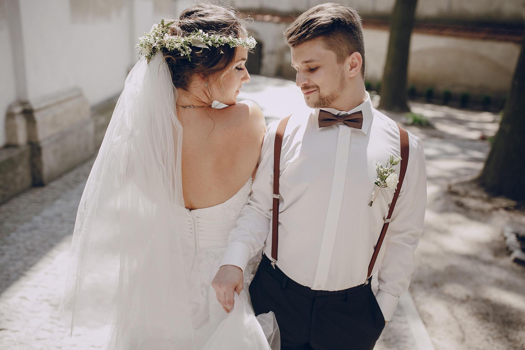 Piękna Panna Młoda w sukni ślubnej z odkrytymi plecami pozująca z Panem Młodym w brązowych szelkach i brązowej muszce
