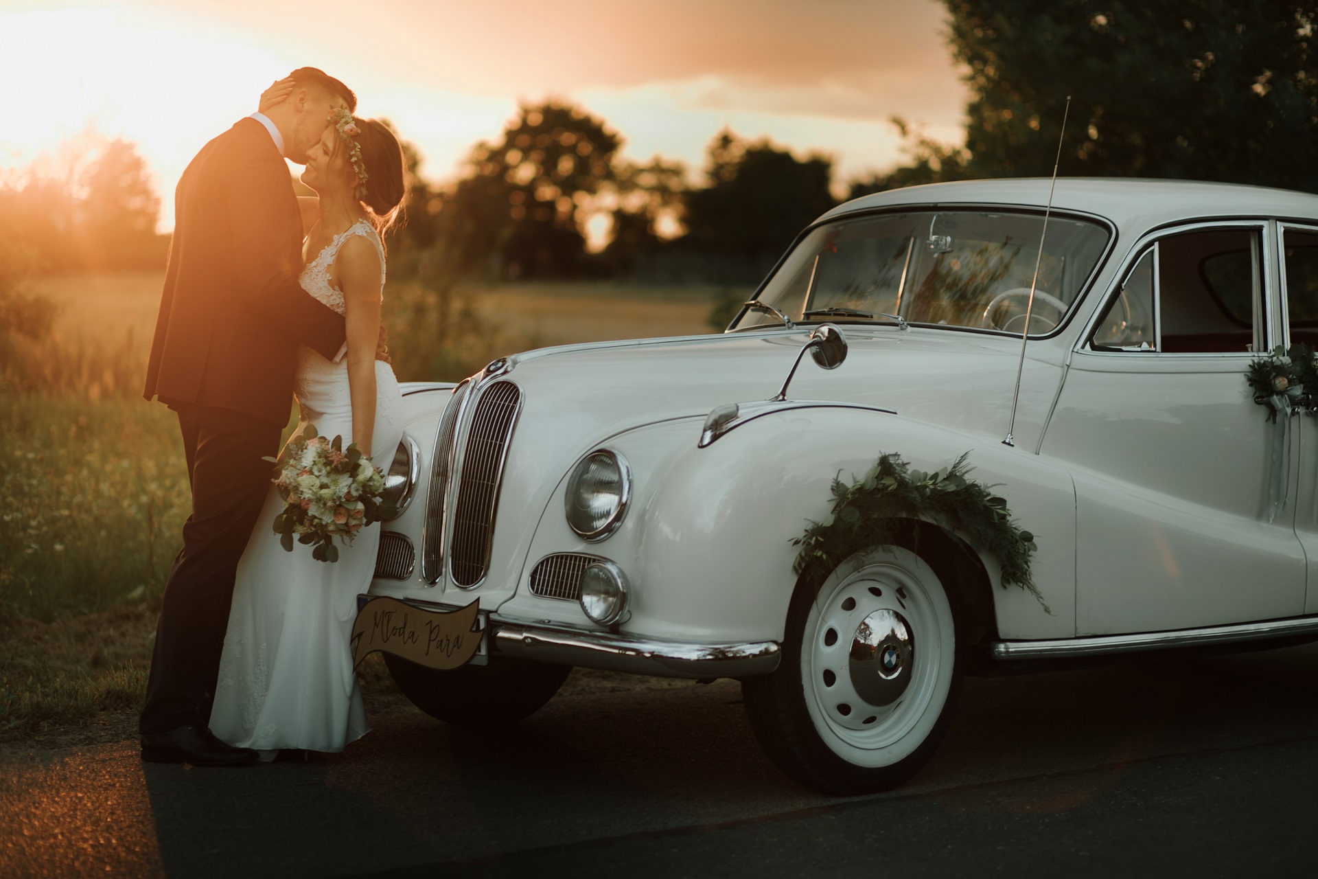 Para Młoda opierająca się o białe auto ślubne