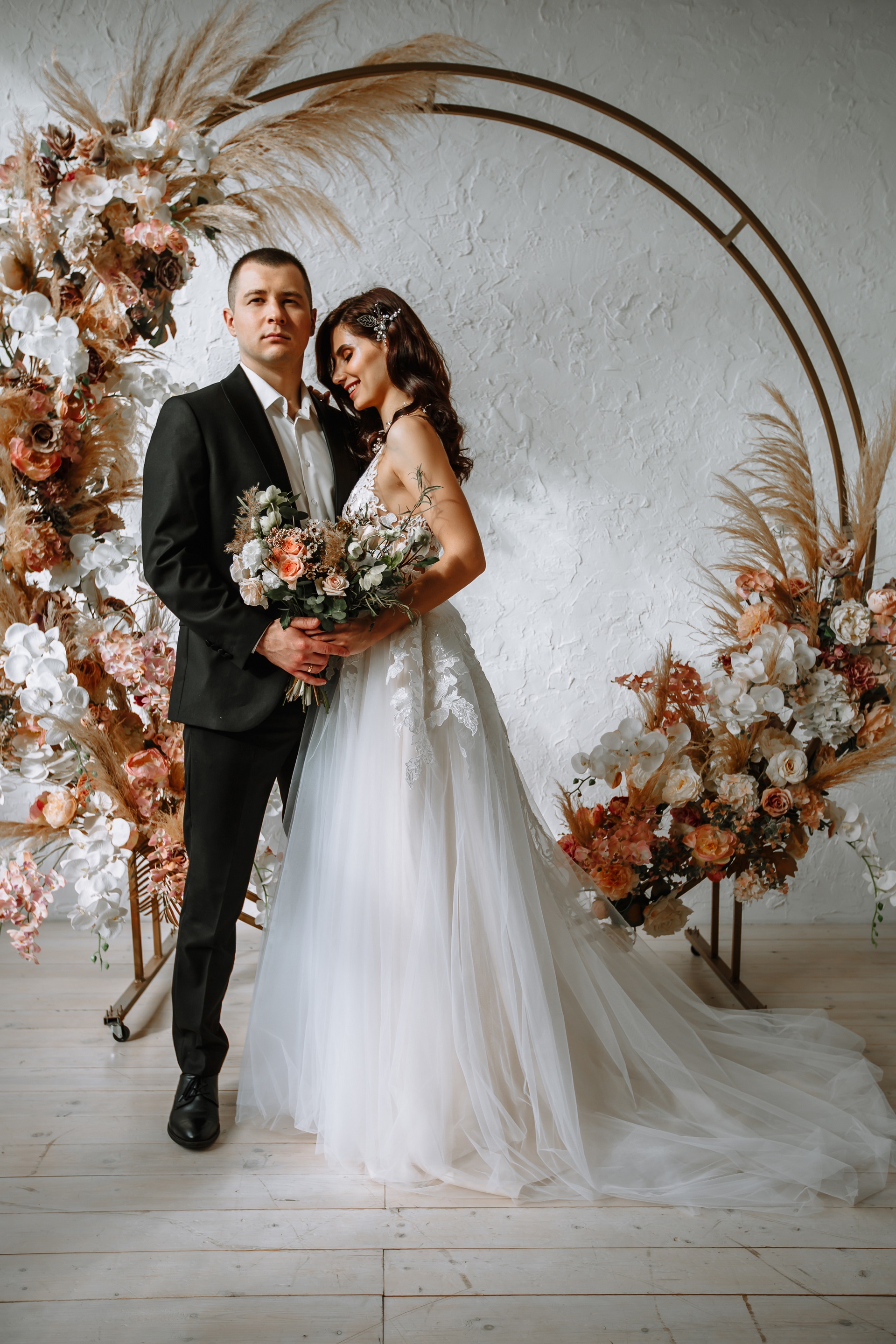Para Młoda w stylu boho na tle okrągłej dekoracji ozdobionej trawami pampas i kwiatami