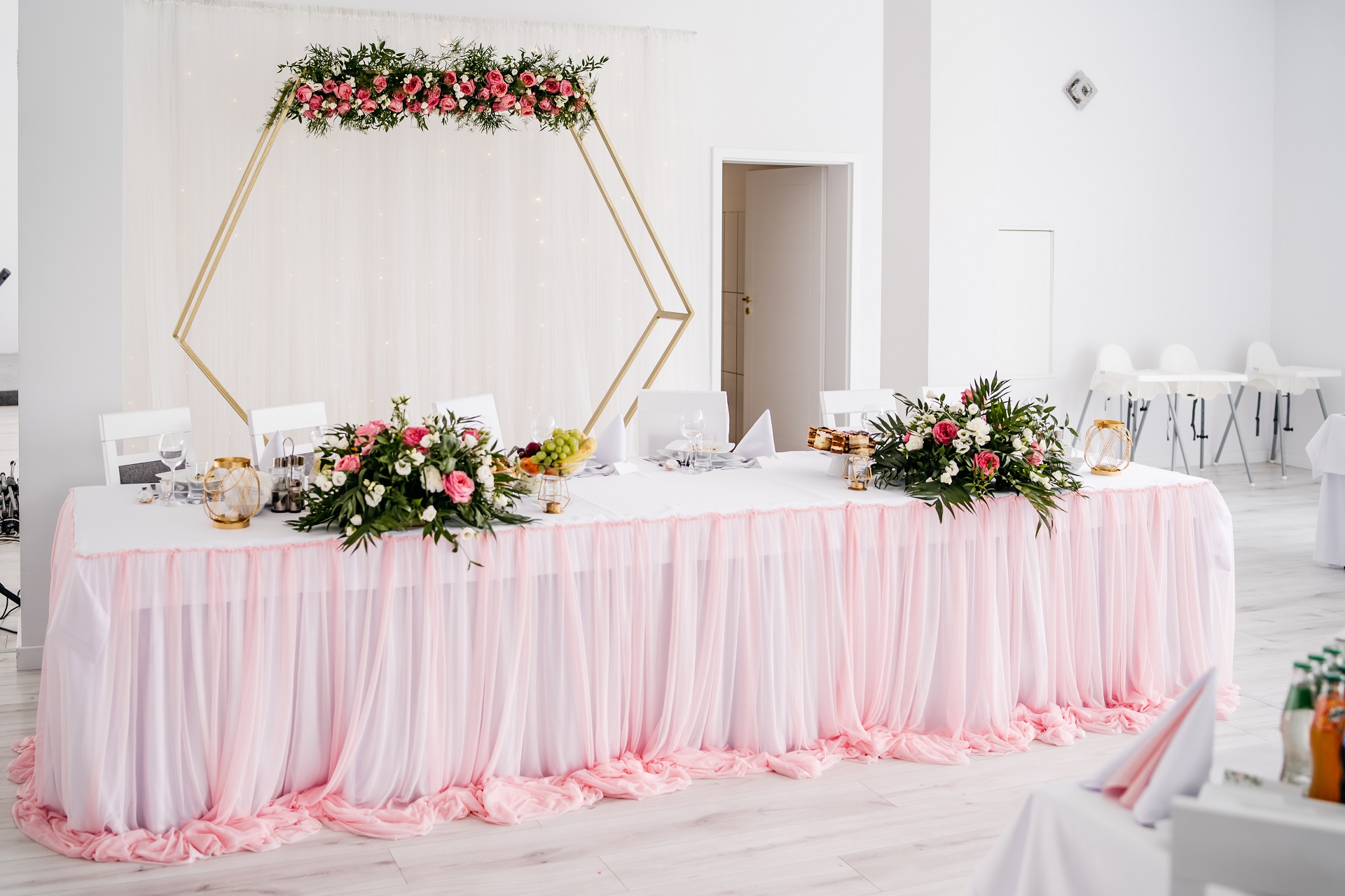 Elegancka ścianka z kwiatami i geometrycznym stelażem za parą młodą, różowe i białe dekoracje stołu pary młodej