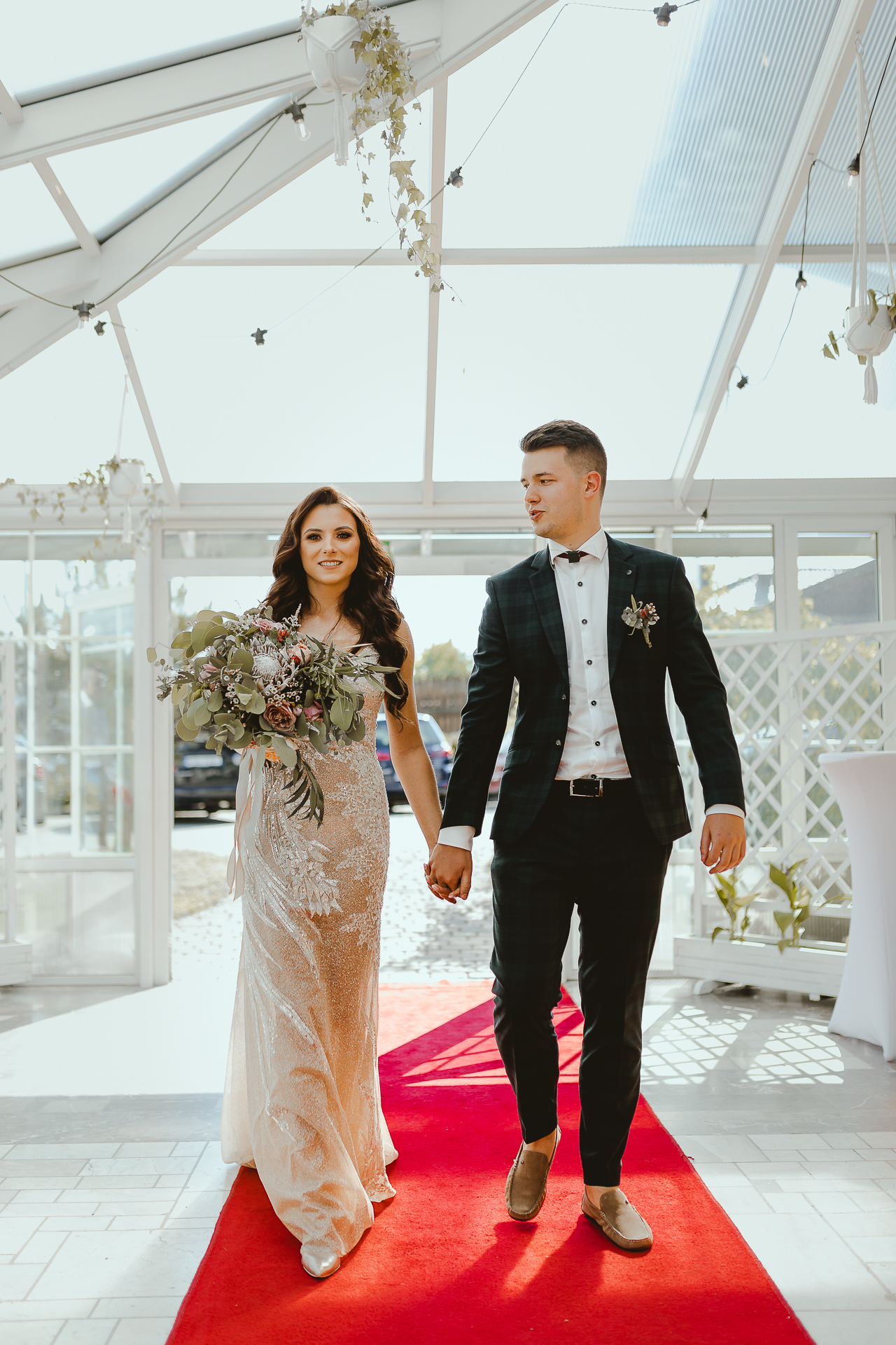 Panna Młoda w długiej dopasowanej eleganckiej sukni ślubnej wraz z Panem Młodym wchodzą na wesele w eleganckim namiocie 