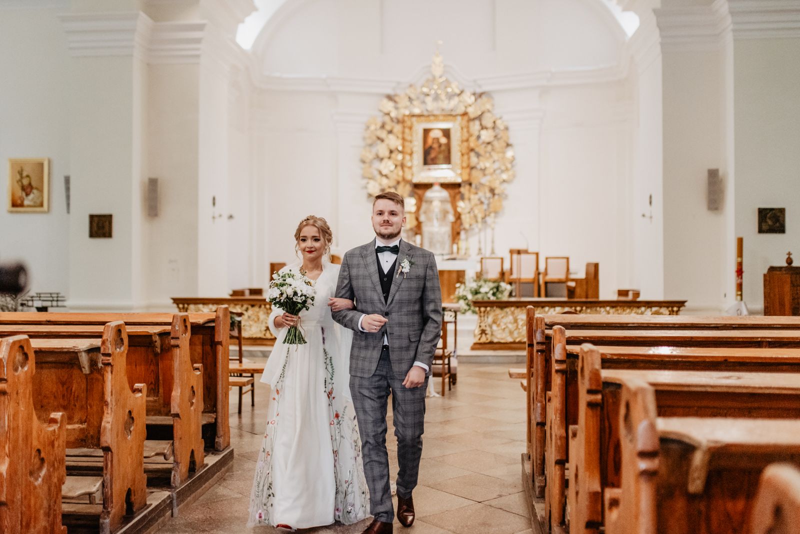 Panna Młoda w sukni ślubnej w kwiaty, Pan Młody w garniturze w kratę wychodzą w kościoła reportaż ślubny