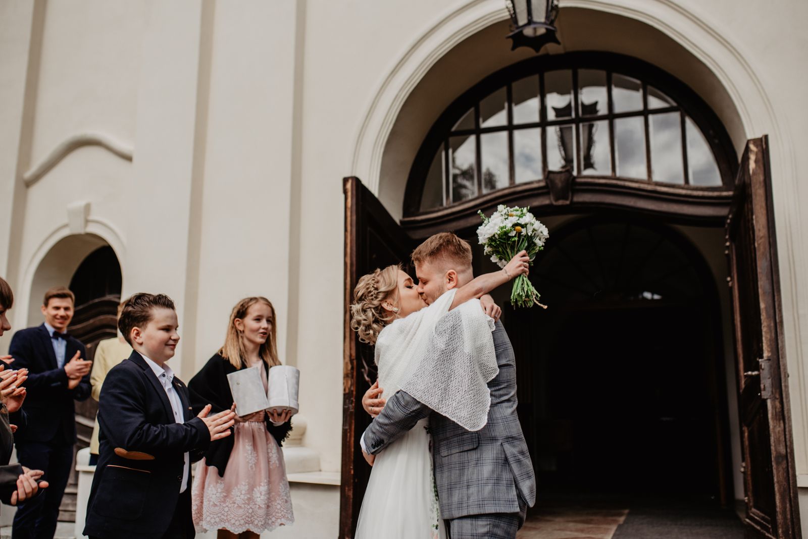 Panna Młoda w sukni ślubnej w kwiaty, Pan Młody w garniturze w kratę wychodzą w kościoła reportaż ślubny