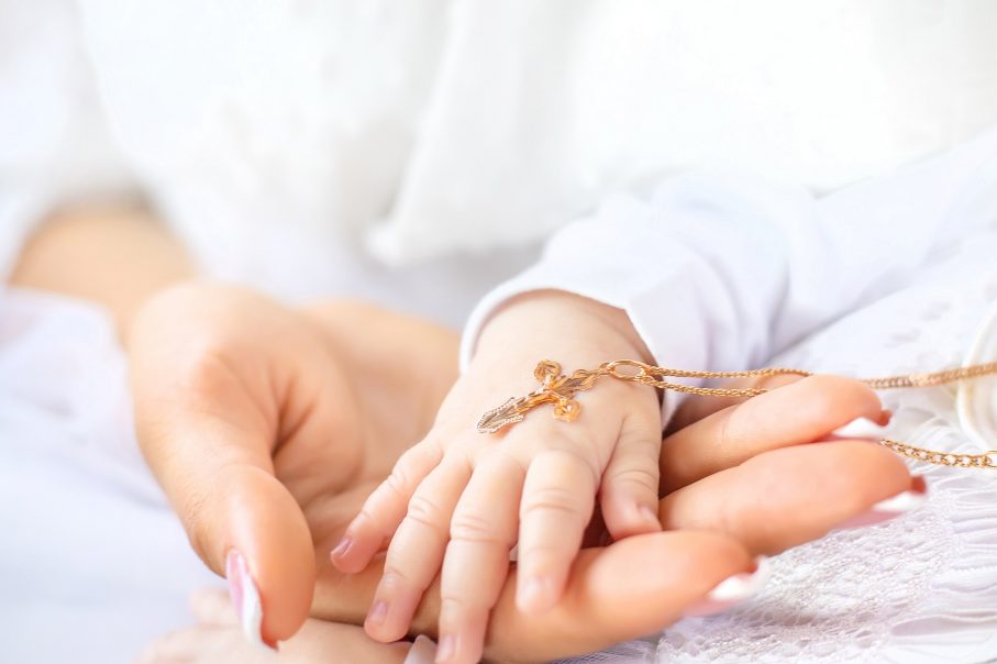 ślub i chrzest jednego dnia. Krzyżyk leżący na dłoni dziecka. Dłoń dziecka położona na dłoni kobiety.